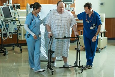 A patient, using a walker, is aided by his clinicians after exiting a TotalCare Bariatric Plus Hospital Bed.
