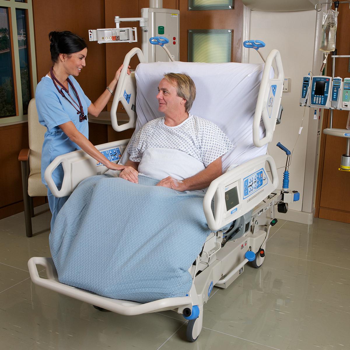 A patient sitting in the TotalCare SpO2RT 2 ICU Bed is comforted by his clinician