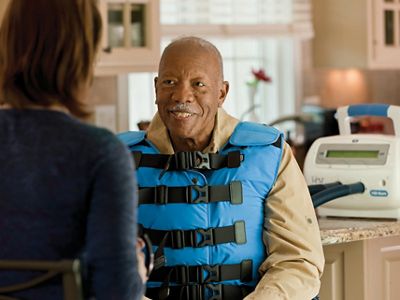 A man smiles while a Hillrom clinical trainer teachers him to use The Vest® System, Model 105 in his kitchen