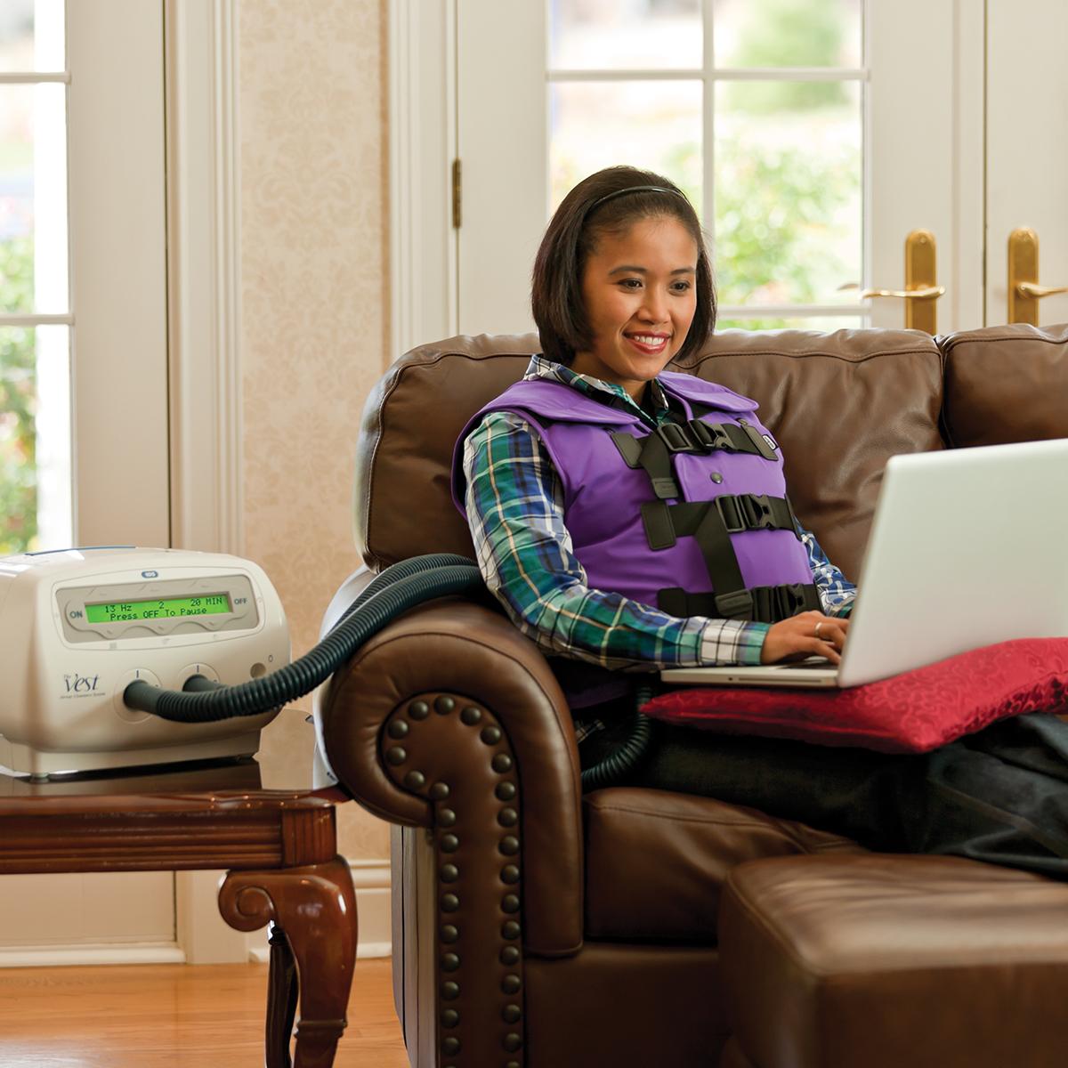 한 젊은 여성이 Color ME Purple 재킷의 The Vest 시스템을 착용하고 컴퓨터로 작업하고 있습니다.