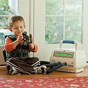 Um menino brinca com caminhões de brinquedo enquanto usa o sistema Vest em casa com um colete Cool Camo.