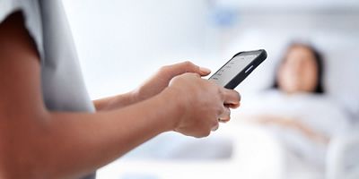 Patient waiting in bed with nurse using mobile