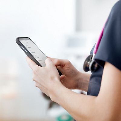 Eine Ärztin liest in einem Patientenzimmer eine Nachricht auf ihrem Smartphone