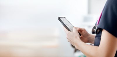 A clinician reads a message on her smartphone in a patient’s room