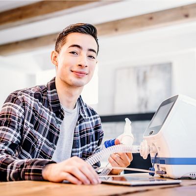 A young man smiles in his home with the Hillrom Volara System nearby, holding the mouthpiece