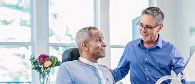 A Hillrom trainer helps a man use the Synclara Cough System at home with a tracheostomy adapter