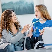 A mother helps her daughter receive OLE respiratory therapy from a Hillrom Volara System through its tracheostomy interface