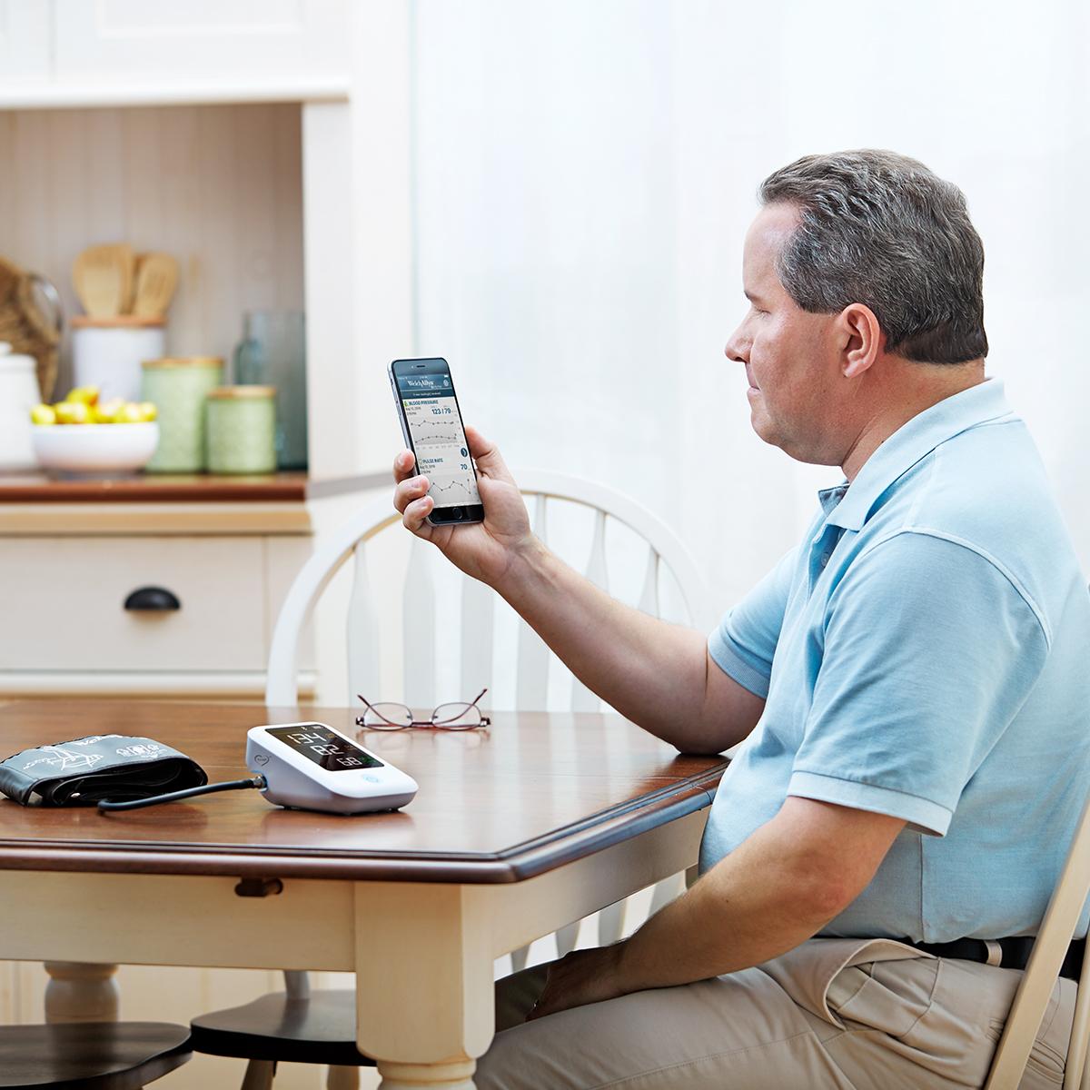 Patient sitting at table, using Welch Allyn Home Hypertension Program on smartphone