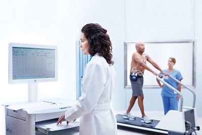 Un médecin examine les résultats d'épreuve d'effort sur un poste de travail Xscribe System avec un patient sur un tapis roulant en arrière-plan