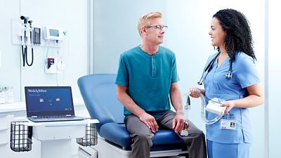 Clinician holding a WAM stands next to a patient and the Welch Allyn Diagnostic Cardiology Suite ECG. 