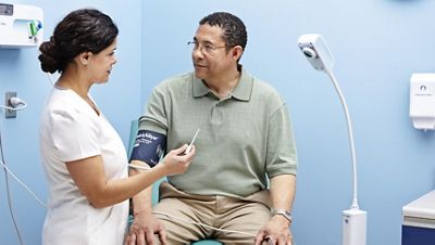 A nurse talks to a patient in an exam room where a Green Series touchless medical light can be seen in the background.