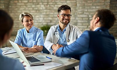 Man in a suit shaking hands with a clinician at a meeting table 