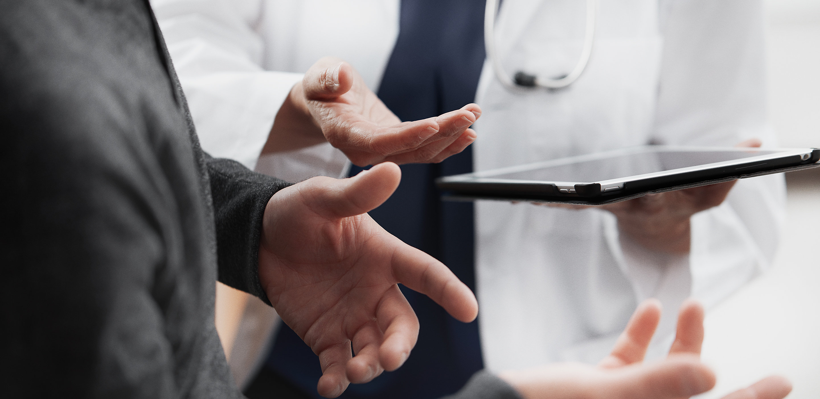 Een arts deelt gegevens op een tablet met haar patiënt. Handen worden in een actief gesprek weergegeven.