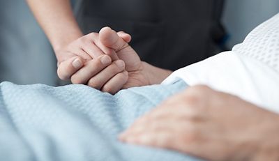 Close-up on a clinician holding the hand of a patient in a Centrella Smart+ bed