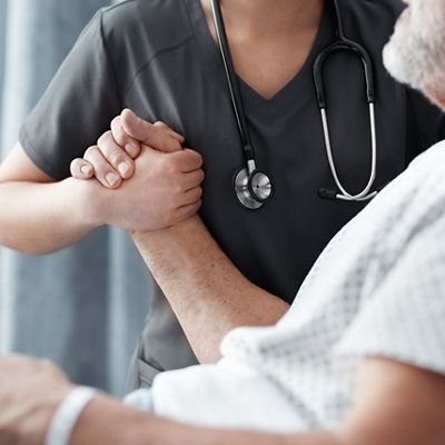 Eine Ärztin umschließt die Hand eines Patienten und unterstützt ihn beim Aufsetzen im Bett