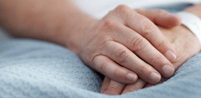 A patient’s hands rest peacefully on top of his blanket in a hospital bed