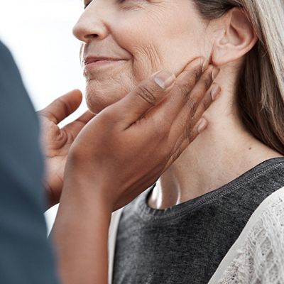 Ein Arzt tastet während einer Untersuchung die Lymphknoten am Hals und an der Kehle einer Patientin ab