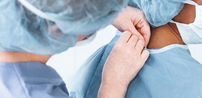 A surgical care team helps each other tie their surgical gowns to prepare for surgery