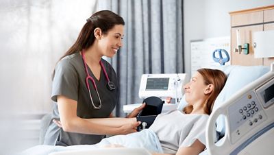 Eine Krankenhausärztin lächelt, während sie den Blutdruck eines Patienten mit dem Connex Spot Monitor misst