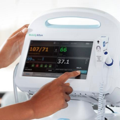 Clinician talking to patient in the background with Connex Vitals Management Software appearing on a desktop computer screen in the foreground 