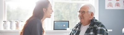A smiling clinician talks with her older patient in an examination room.