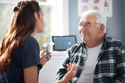 A clinician coaches a patient on how to blow into their spirometer during an exam with the Diagnostic Cardiology Suite Spirometry. 