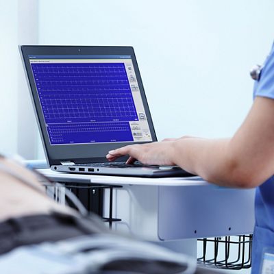 A clinician types on a laptop with the Welch Allyn Diagnostic Cardiology Suite software while a patient exam takes place. 