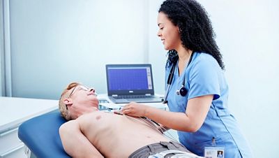 A smiling caregiver places resting ECG leads on her patient. Diagnostic Cardiology Suite software is shown in the background.