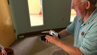 a man smiles and holds the Spot Vision Screener in a dimly lit room