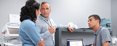 A group of technicians converse around a workstation.