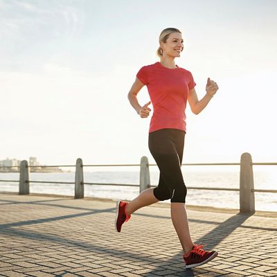 A smiling woman runs along a waterfront.
