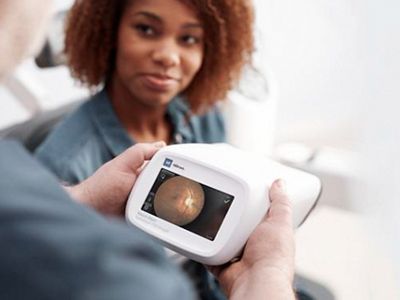 A clinician looks at the results of a retinal exam on the Welch Allyn® RetinaVue® 700 Imager while the patient smiles.