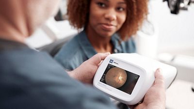 A child sits on his mother's lap while his vision is screened with the Welch Allyn Spot Vision Screener in a primary care exam room.
