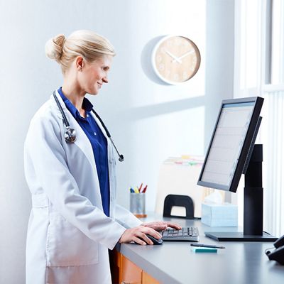 A physician smiles while reviewing patient data on a desktop computer monitor