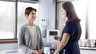 A nurse comes back to visit her patient after the Spot Vital Signs® 4400 Device performed an automatic blood pressure averaging exam. 