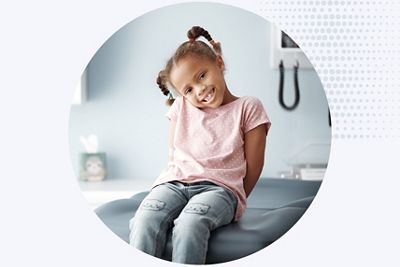 a young girl smiles on an exam table in a primary care setting
