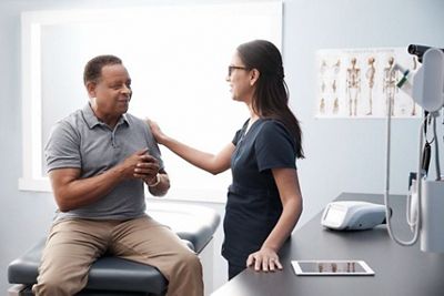 A clinician engages in conversation with a patient, resting her hand on the patient’s shoulder. The Welch Allyn® RetinaVue® 700 Imager sits on the counter next to them.