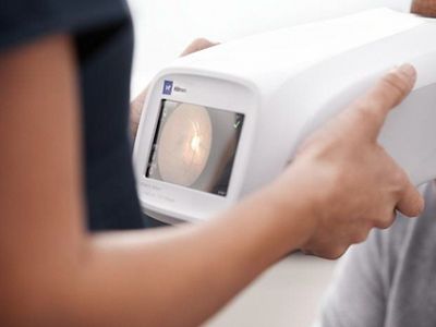A clinical holds the Welch  Allyn® RetinaVue 700 Imager up to the patient’s eyes to perform a diabetic retinal exam.