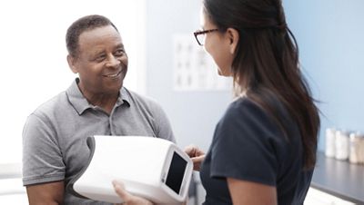 A nurse speaks to a diabetic patient before an eye exam while holding the RetinaVue 700 Imager in her hand.