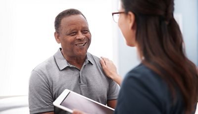 A clinician holding a tablet device speaks with her patient in the exam room.