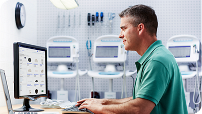 Biomed professional working at a desktop computer to manage and monitor medical equipment in a lab setting.