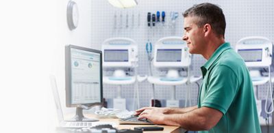 A biomed reads information on a computer screen. Tools and Connex® Vital Signs Monitors are in the background 