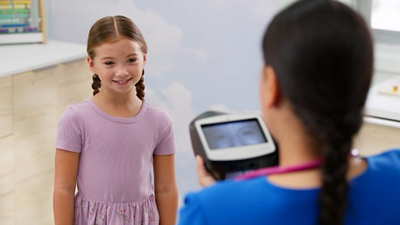 girl smiling looking at nurse holding the spot vision screener