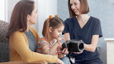 A smiling child sits with her mom while a nurse is showing her the Welch Allyn Spot Vision Screener device