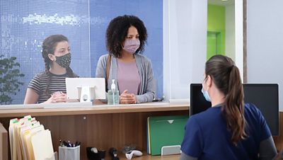 A mother and daughter stand behind the front desk of an urgent care clinic.