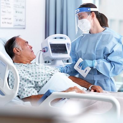 A doctor wearing gloves, surgical mask, and face shield checks on elderly patient in hospital setting