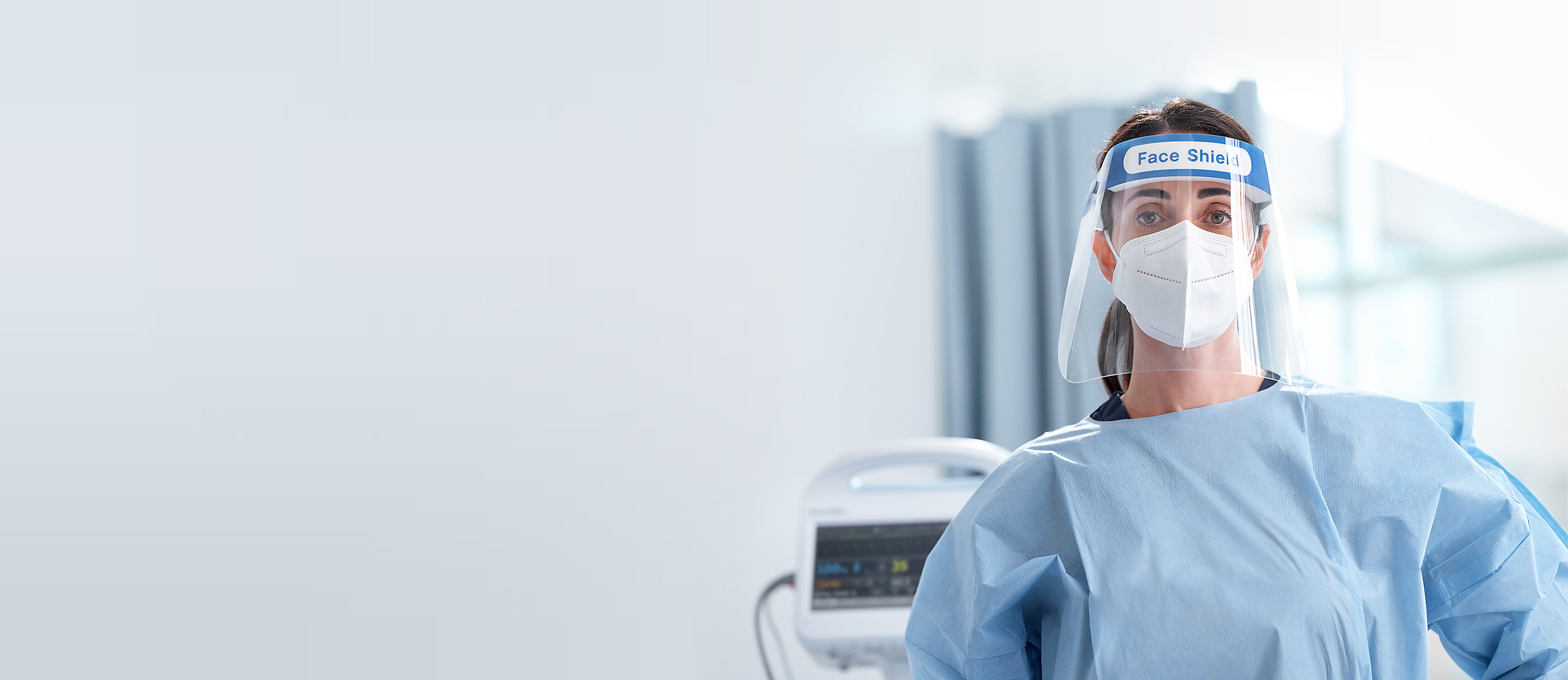 Female clinician wearing PPE stands in front of a Welch Allyn Connex Vital Signs Monitor. 