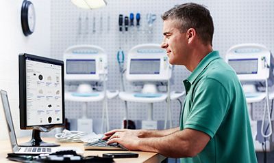 A biomed reads information on a computer screen. Tools and Connex® Vital Signs Monitors are in the background