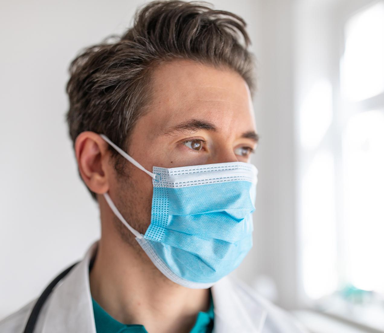 A hospital clinician wearing a mask is deep in thought